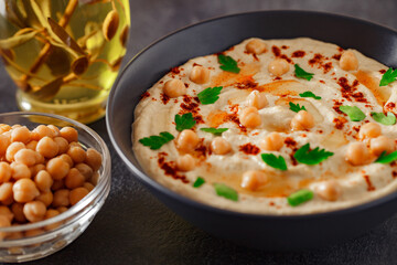 Hummus with chickpeas, oil, spices and herbs in bowl on dark background, selective focus