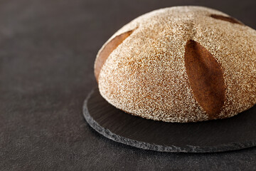 Fototapeta na wymiar Dark bread sprinkled with semolina, on slate stone plate round, dark background, selective focus
