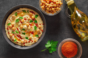 Hummus with chickpeas, oil, spices and herbs in bowl on dark background, top view.