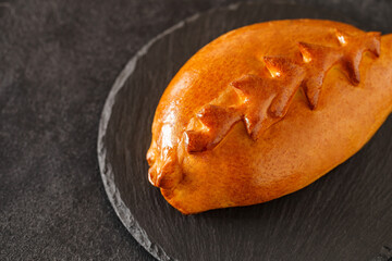 Pie closed with baked pigtail of dough, on slate stone plate round, dark background, selective focus