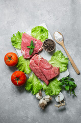 Raw beef steak meat on cutting board on rustic background with mint leaves, peppers and lettuce, butcher concept