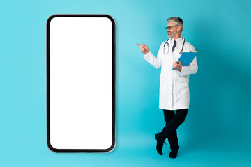 Positive middle aged man doctor showing huge phone with mockup