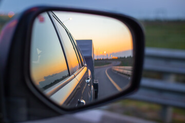 View in the side mirror of a moving car on the road and the sunset in the sky
