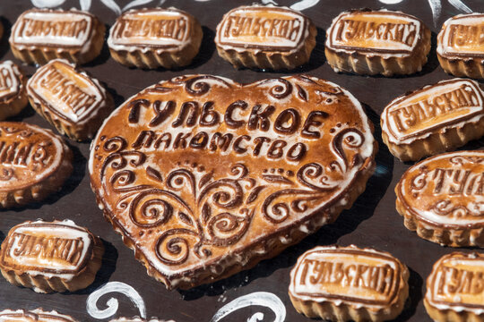 Group of stamped Tula pryaniks (russian traditional gingerbread with honey or jam) lies on souvenir shop showcase. Russian text translation: "Tulsky" (from Tula) and "Tula delicacy". Soft focus.