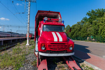Red fire engine pulls out of freight covered wagon on railway station in a summer sunny day. No...