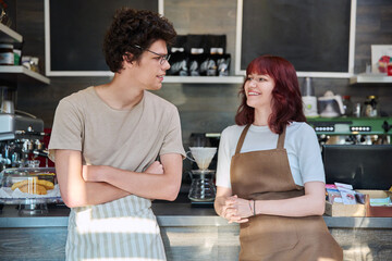 Young coffee shop workers talking, standing in front of counter in cafeteria