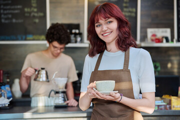 Portrait of young female waitress in front of counter in coffee shop