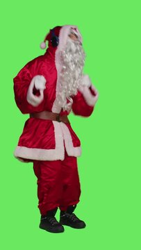 Vertical video Side view of santa claus using audio headset to listen to music and have fun during christmas eve holiday, full body greenscreen backdrop. Saint nick cosplay in costume dancing on songs