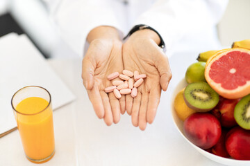 Adult european woman doctor nutritionist in white coat at table with organic fruits and juice holds pills in hands