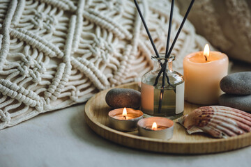 Fototapeta na wymiar Burning candles on bamboo tray, cozy home atmosphere. Relaxation, detention zone in the living or bedroom. Stones, sea shells as decor. Apartment natural aroma diffusor with ocean breeze fragrance.