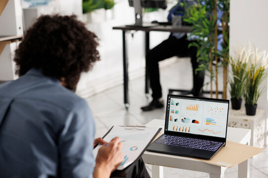 Entrepreneur preparing financial reports and analyzing market data on laptop screen while sitting in coworking space. Company analyst checking performance metrics and sales roi