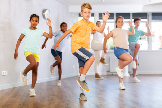 Dynamic little boy training Hip hop dance poses in dancehall with other attendees of dancing courses