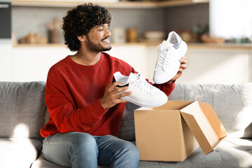 Portrait of happy young indian man unboxing parcel with shoes at home - obrazy, fototapety, plakaty