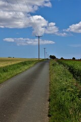 Fototapeta na wymiar Long country road with telegraph poles against a blue sky with some white clouds