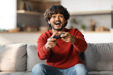 Young happy indian man laughing and playing video games on weekend
