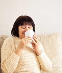 Good looking relaxed senior woman in good mood drinking a cup of coffee or hot tea at home.