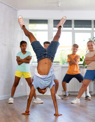 Positive juvenile boy engaged in Breakdancing together with children's group in training room during workout session