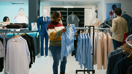 Diverse women talking about fashion brands in retail shop, client and store assistant looking at modern new collection. Two people analyzing clothing store merchandise at mall.