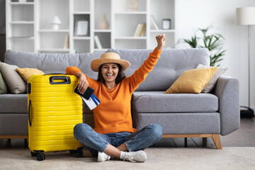 Thrilled indian woman with suitcase, passport and tickets, home interior