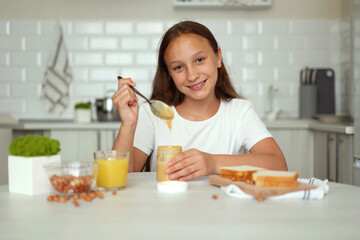 A girl in a good mood making a peanut butter sandwich in the kitchen