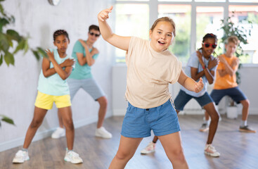 Positive girl dances waacking in choreographic school, group of young people in sportswear trains together with their classmates in gym before competitions, battle