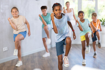 Portrait of expressive happy african-american tween boy practicing energetic dance movements with group of children in choreography class ..