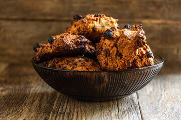 Homemade oatmeal cookies in a glass dark bowl on a wooden table.