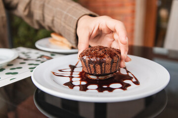 Hands of a girl lifting a chocolate cupcake, in an outdoor cafe.