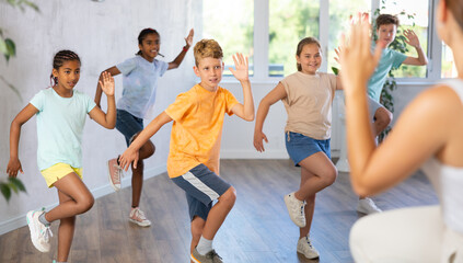 Boy moves to beat of music in dance lesson and repeats movements behind unrecognizable teacher. Multi-racial group of children performs workout in studio