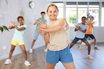Portrait of cheerful preteen girl enjoying active dancing during group training in dance studio..