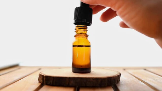 A bottle of cosmetic oil for skin care in the white background. Holds a pipette with medicinal oil. Alternative medicine, vitamins C and squalene, cosmetic serum, hyaluronic acid. Dark brown glass.