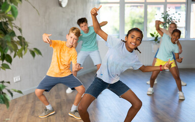 Dynamic little boy training Break-dance poses in dancehall with other attendees of dancing courses