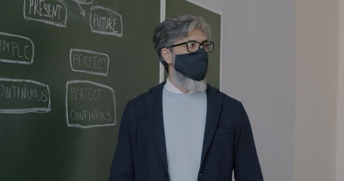 Portrait of English teacher wearing face mask explaining grammar working in classroom during covid-19 pandemic. People and healthcare concept.