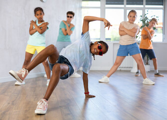 Expressive cheerful african american tween boy practicing hip-hop movements during group dance...