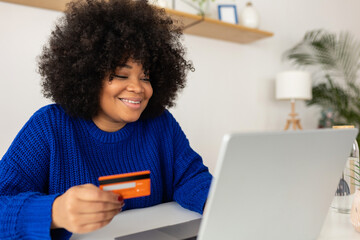 Latina beautiful woman buying online using credit card and laptop computer sitting on table at home. Online shopping and electronic banking concept.