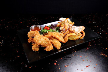 Fried chicken strips with vegetables and sauce on a black plate.
- 619607346