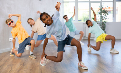 Positive juvenile boy engaged in Breakdancing together with children's group in training room...