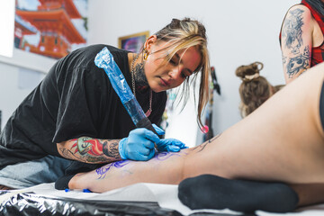 tattoo artist drawing on a client's leg lying on the table, art studio. High quality photo