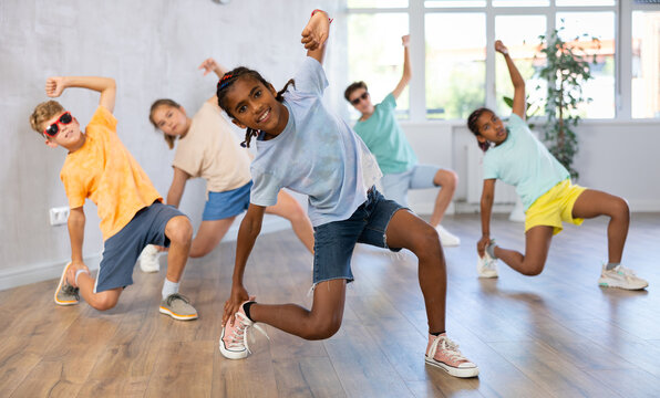 Positive juvenile boy engaged in Breakdancing together with children's group in training room during workout session