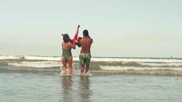 Mother and Father playing and fooling around with his toddler son at the ocean beach having fun. Multi ethnic family playing with his young son at the beach, priceless parenthood moments.
