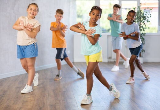 African girlie performs movements during warm-up, limbering-up part of workout together with peers. Group of young girls and guys dance modern waacking in fitness club unfocused