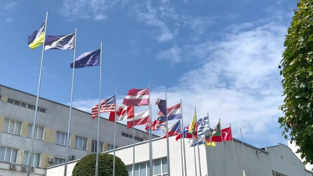 Many flags of different countries against the background of government buildings and blue sky. Flagpoles.