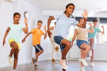Fototapeta premium Positive juvenile boy engaged in Hip-hop dance together with children's group in training room during workout session