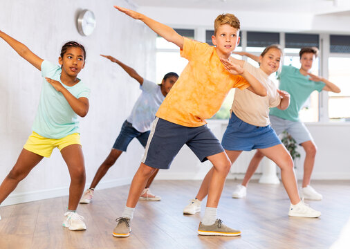 Emotional cheerful tween boy enjoying contemporary dance with group of children, showcasing dabbing move..