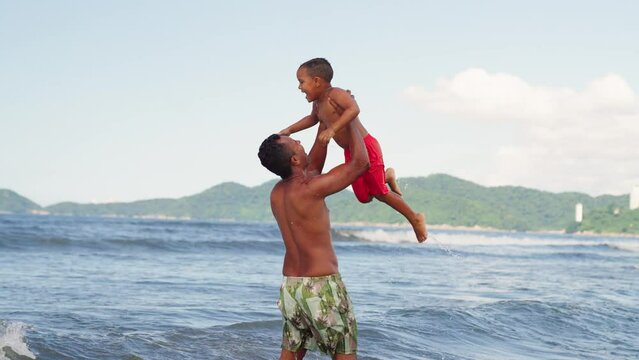 Dad playing and fooling around with his toddler son at the ocean beach having fun. Multi ethnic father playing with his young son at the beach, priceless parenthood moments.

