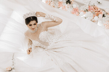 a young girl with a beautiful hairstyle and makeup in a luxurious wedding dress and a tiara on her...