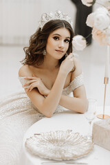 studio photo of a princess in a wedding dress with a luxurious hairstyle and makeup, the bride is sitting at the table © Vasil