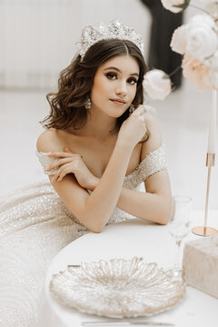 studio photo of a princess in a wedding dress with a luxurious hairstyle and makeup, the bride is sitting at the table