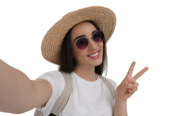 Smiling young woman in sunglasses and straw hat taking selfie and showing peace sign on white background