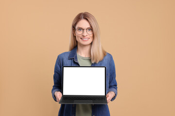 Happy woman showing laptop on beige background